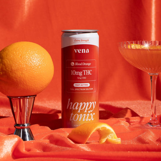 Front view of Vena Blood Orange seltzer can showing 10mg THC and 5mg CBD label and ‘happy tonix’ branding with orange satin backdrop, whole and peeled orange, and a coupe glass