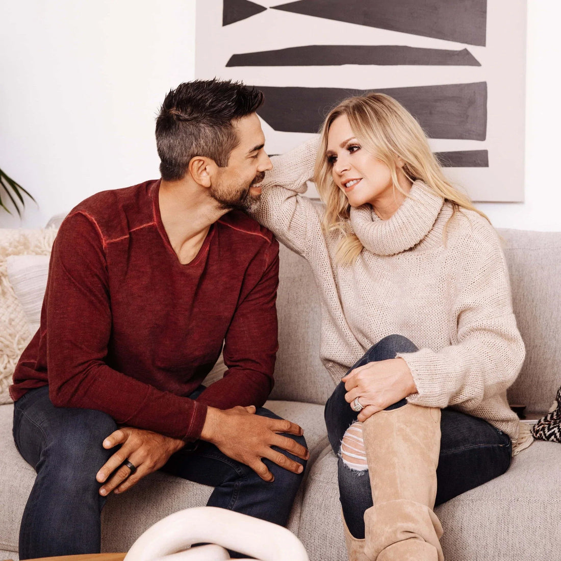 Smiling man and woman sitting on a couch, woman in a turtleneck sweater and boots, casual living-room setting