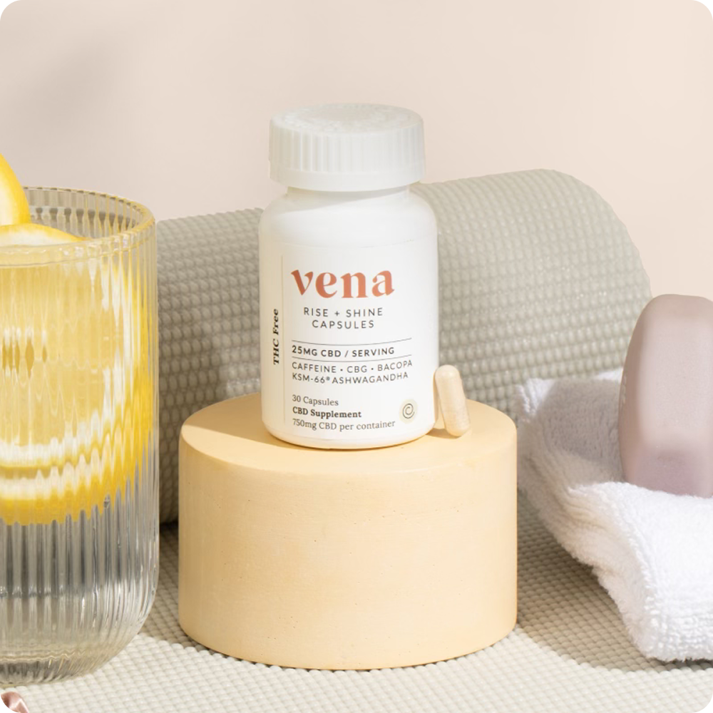 Vena Rise + Shine white capsule bottle on round beige pedestal with one capsule; glass of lemon water and towel nearby