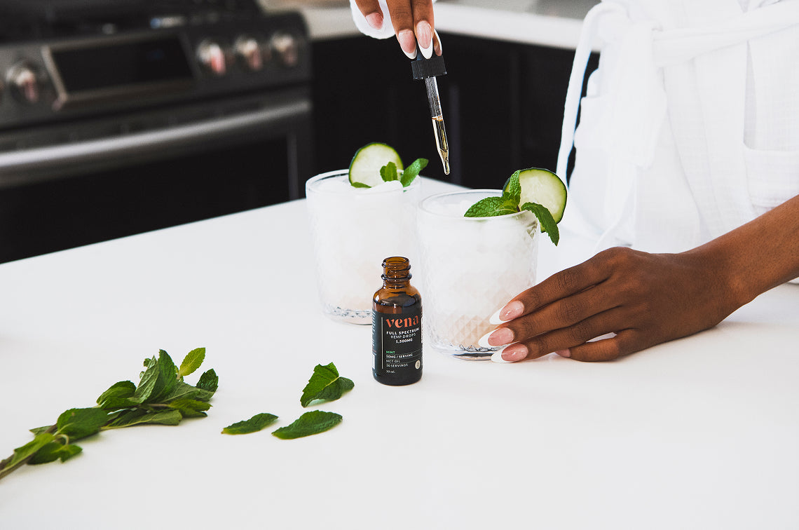 Hand dropping tincture from dropper into iced cucumber-mint drinks; bottle labeled vena FULL SPECTRUM HEMP OIL 1500MG 30ML.