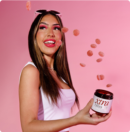 Woman holding jar of xtra bliss gummies as sugar-coated gummies float against a pink background
