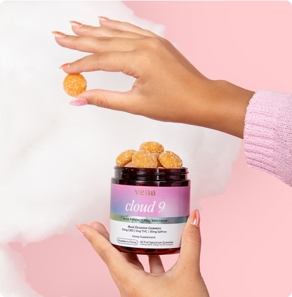 Hands holding a jar labeled vena cloud 9 with sugar-coated gummies; gummy pinched between fingers, pink background