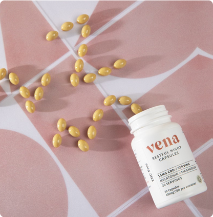Angled close-up of Restful Night CBD + Melatonin bottle showing 15 mg CBD per serving with yellow softgels on pink patterned background