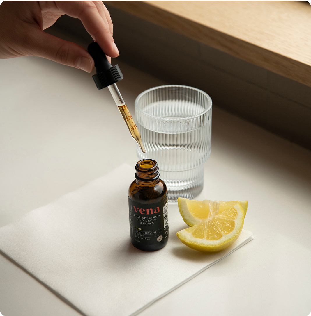 vena CBD tincture bottle with dropper, glass of water and lemon wedges on cloth