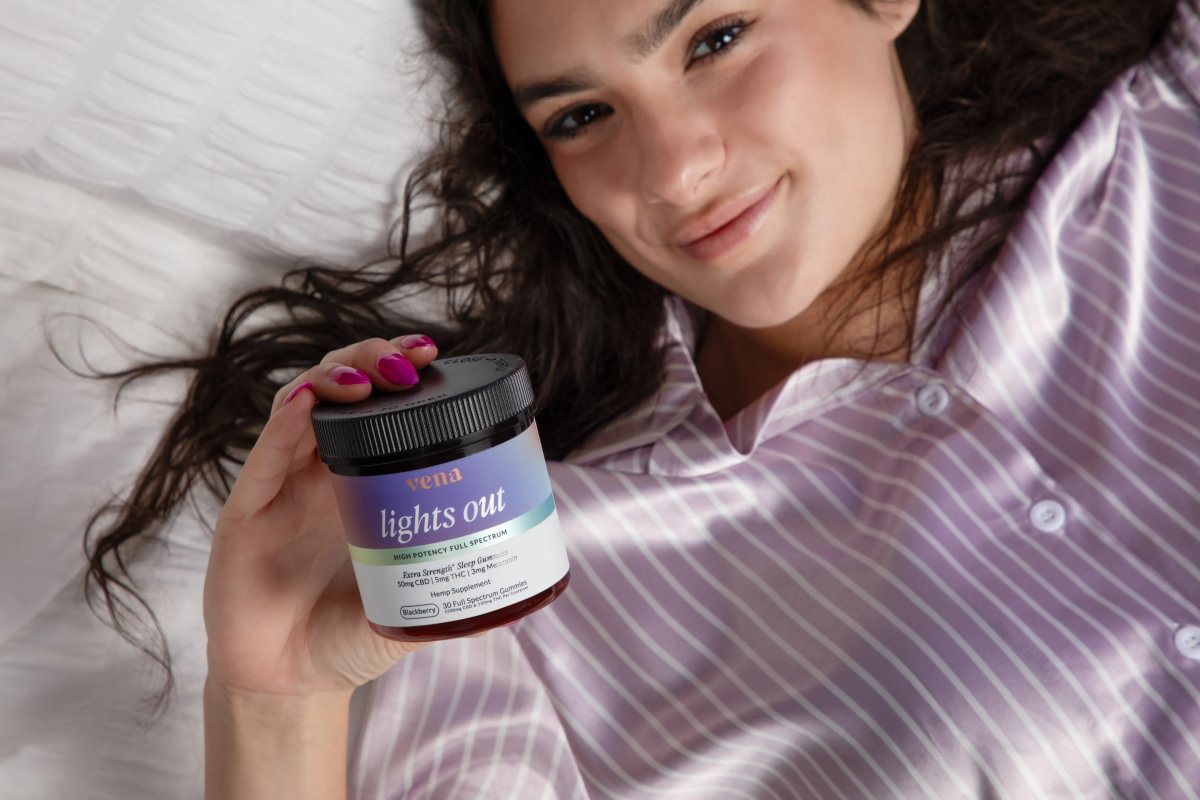 Woman in bed holding a jar of Lights Out sleep gummies