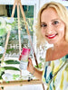 Smiling woman in yellow dress holding a jar with pink label at a wooden market-style display