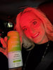 Smiling woman in a car holding up a beverage bottle with a visible label