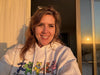 Young woman smiling at camera in white hoodie, warm sunset light coming through window
